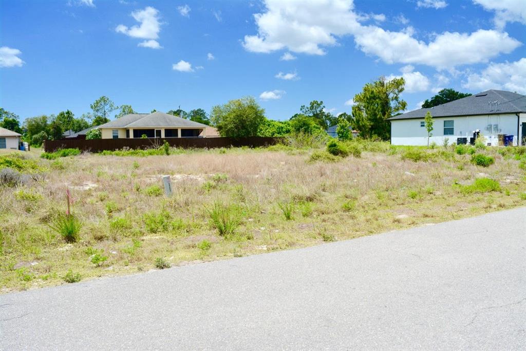 A vacant, grassy residential lot sits next to a paved road with houses in the background — 4505/4507 27TH STREET SW, LEHIGH ACRES, FL