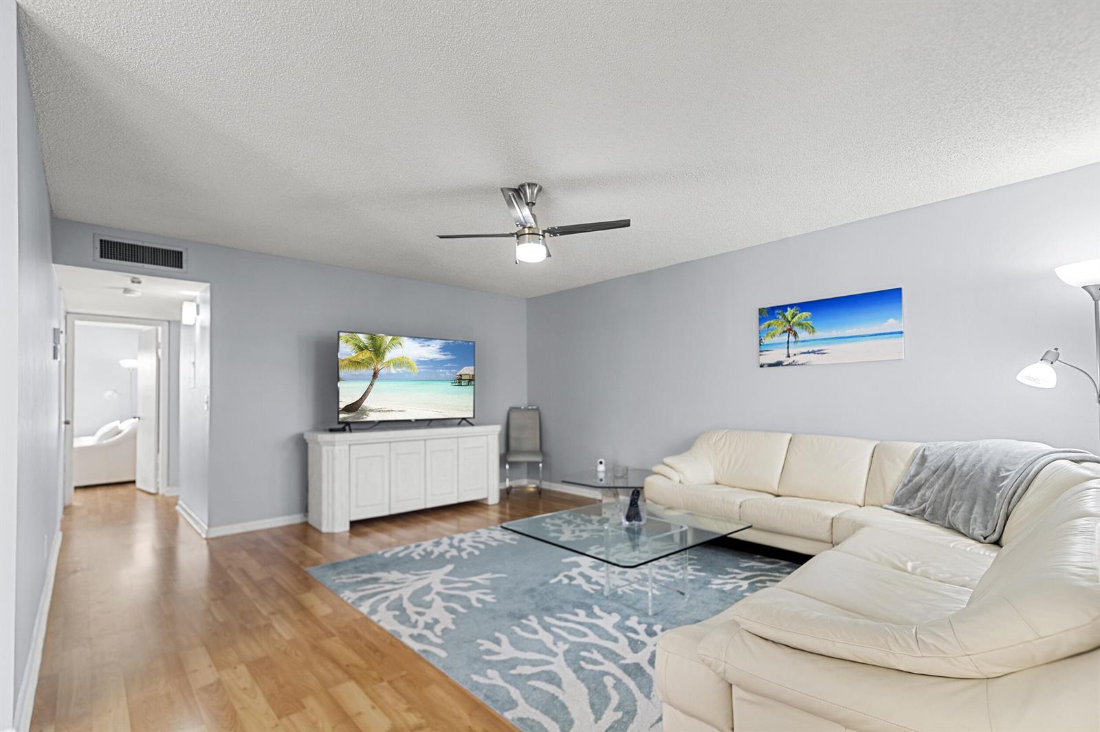 A living room features a white sectional sofa, a glass coffee table, and a television — 605 Flanders M, Delray Beach FL 33484, DELRAY BEACH, FL