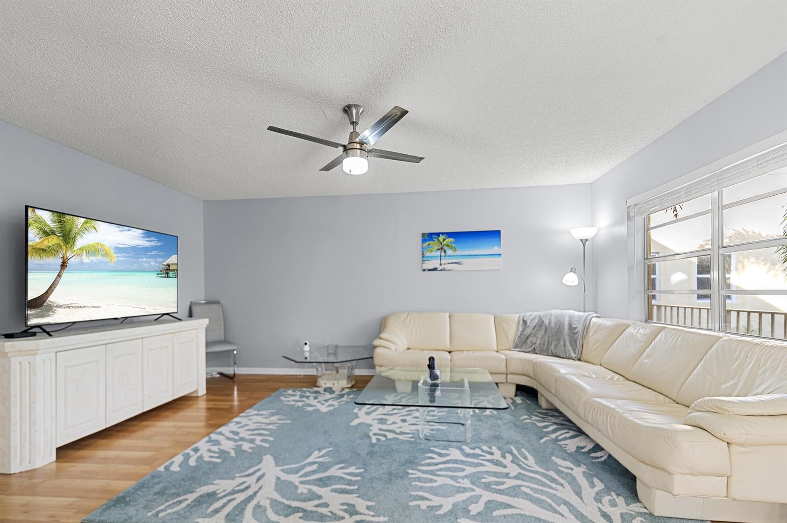 A living room features a white sectional sofa, a coral-patterned rug, and a ceiling fan — 605 Flanders M, Delray Beach FL 33484, DELRAY BEACH, FL