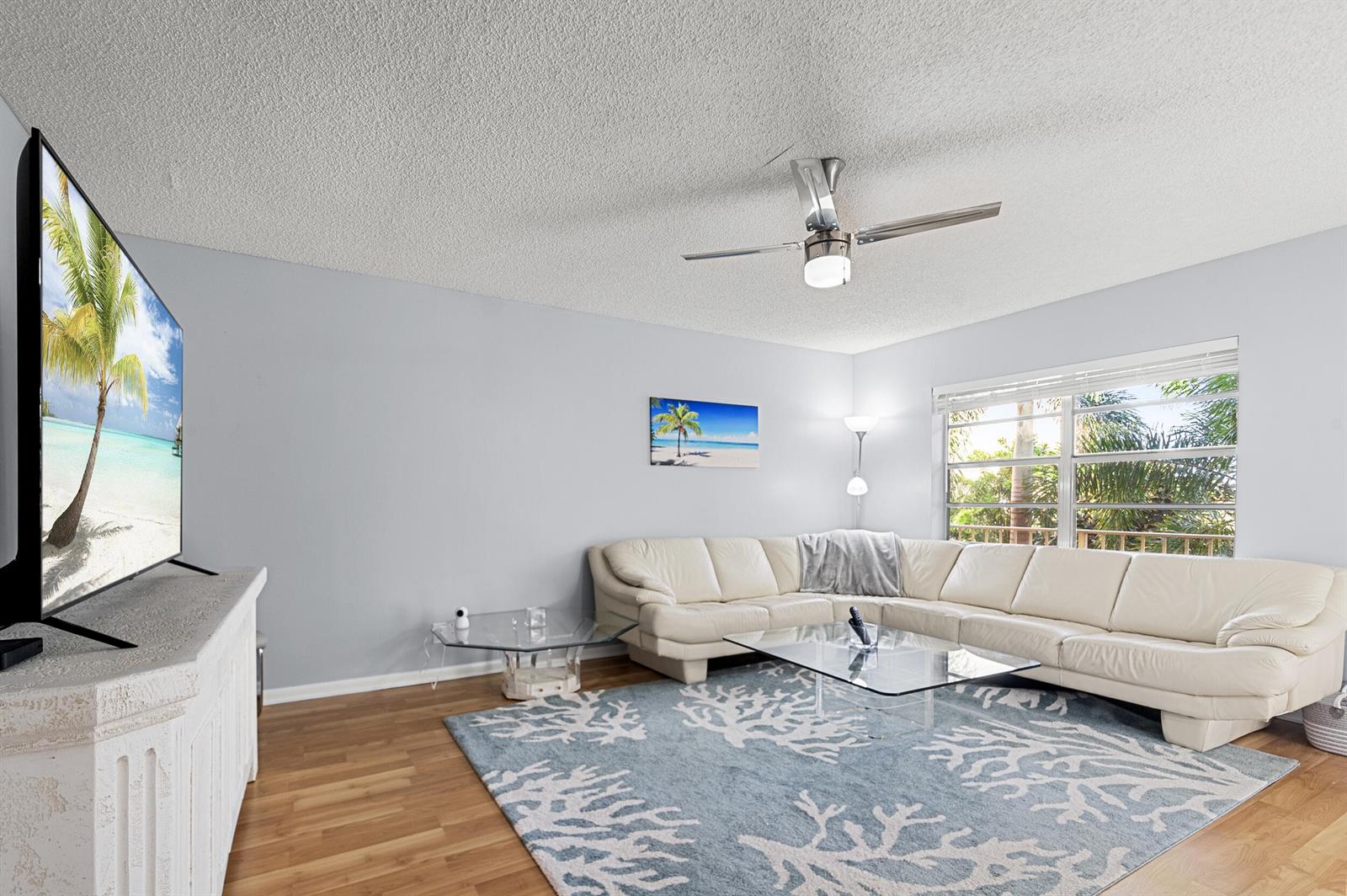 A living room features a white sectional sofa, a glass coffee table, and a coral-patterned rug — 605 Flanders M, Delray Beach FL 33484, DELRAY BEACH, FL