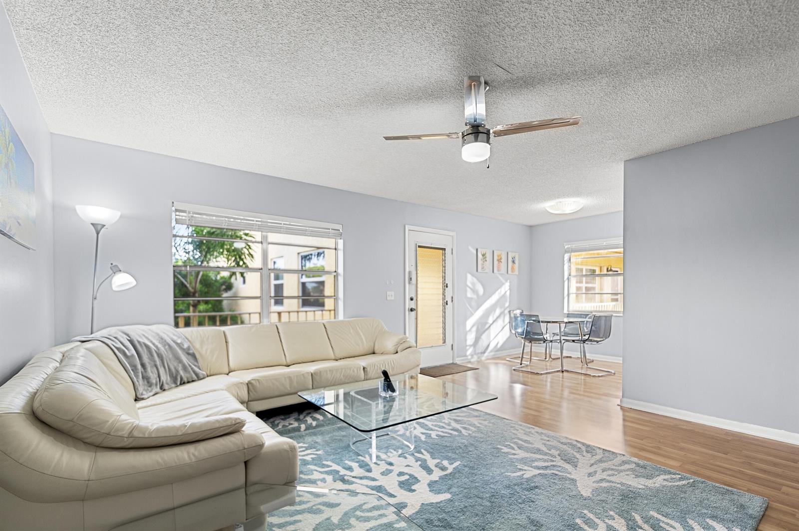 A living room features a white sectional sofa, glass coffee table, and blue patterned rug — 605 Flanders M, Delray Beach FL 33484, DELRAY BEACH, FL