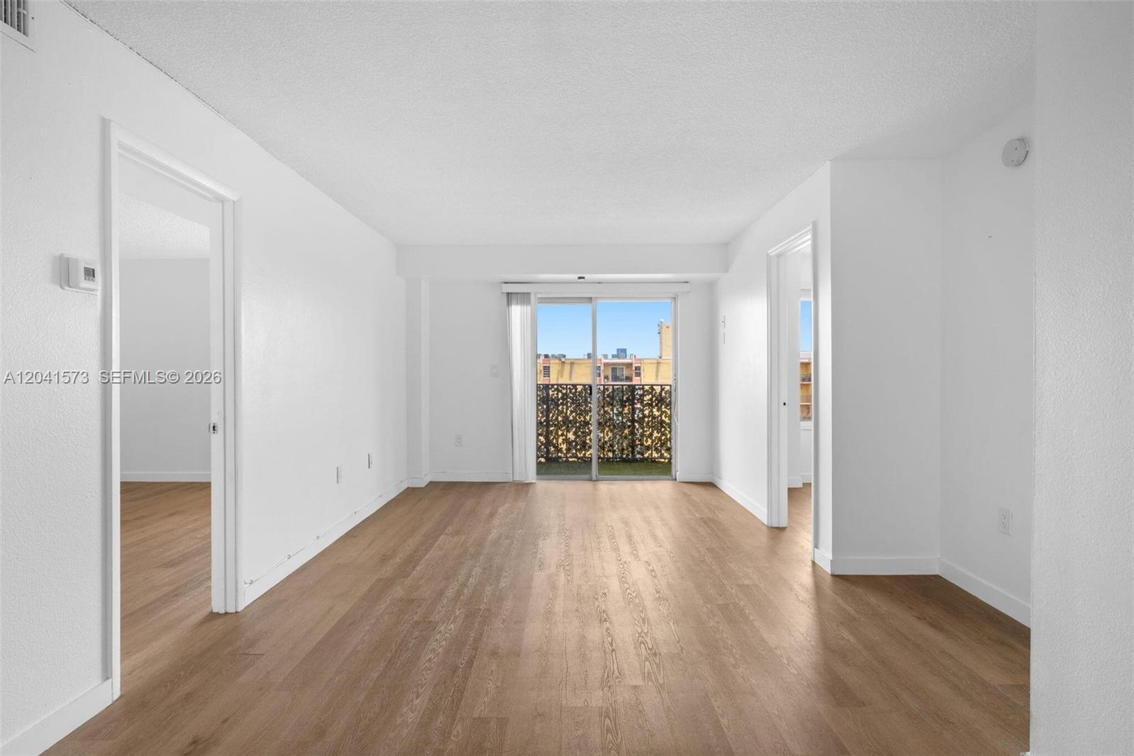 An empty living room features white walls, wood-look flooring, and a sliding glass balcony door — 4801 NW 7th St # 16, Miami FL 33126, MIAMI, FL