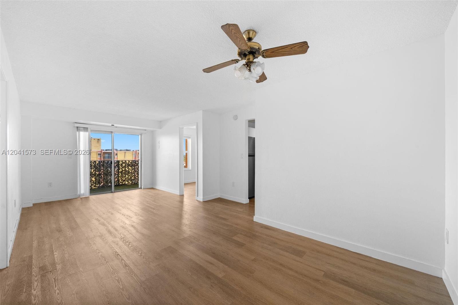 An empty living room features light wood-look flooring, a ceiling fan, and a sliding glass door — 4801 NW 7th St # 16, Miami FL 33126, MIAMI, FL