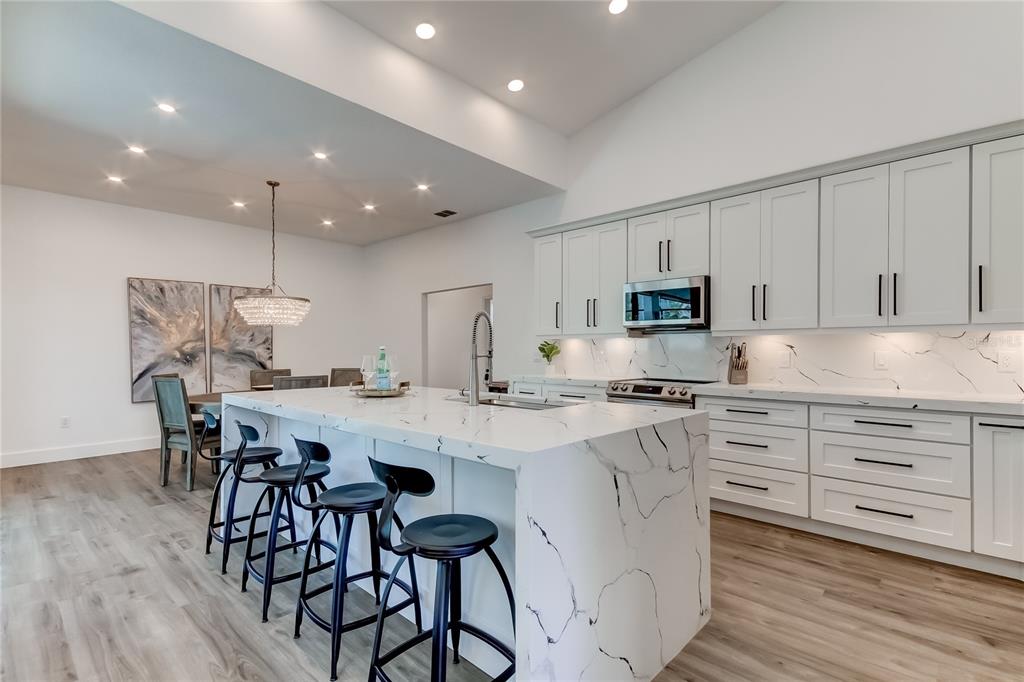 A modern kitchen features a large marble waterfall island, white cabinetry, and light wood flooring — 112 LEEWARD ISLAND, CLEARWATER, FL