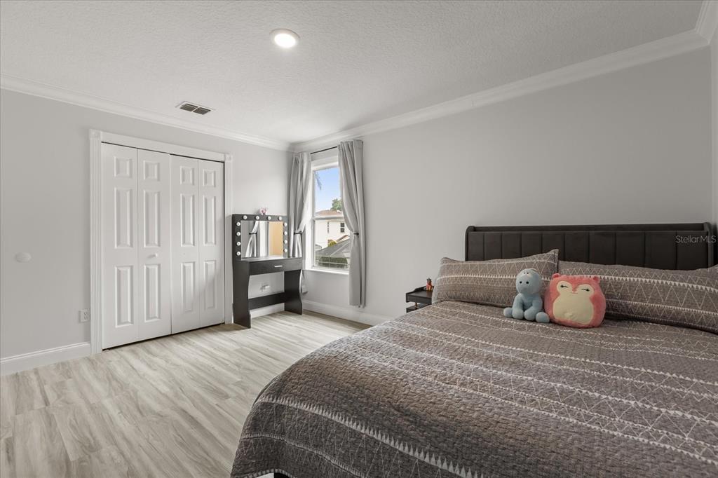 A bedroom features light wood-look flooring, a dark upholstered headboard, and a white vanity table — 1792 GLENHAVEN CIRCLE, OCOEE, FL