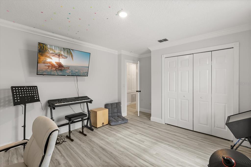 A room with light wood-look flooring, a wall-mounted television, a keyboard, and white closet doors — 1792 GLENHAVEN CIRCLE, OCOEE, FL