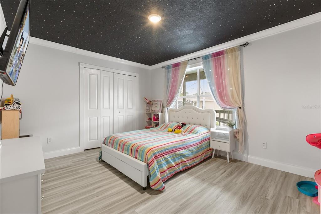 A bedroom features a star-patterned black ceiling, light wood-look flooring, and a striped bedspread — 1792 GLENHAVEN CIRCLE, OCOEE, FL