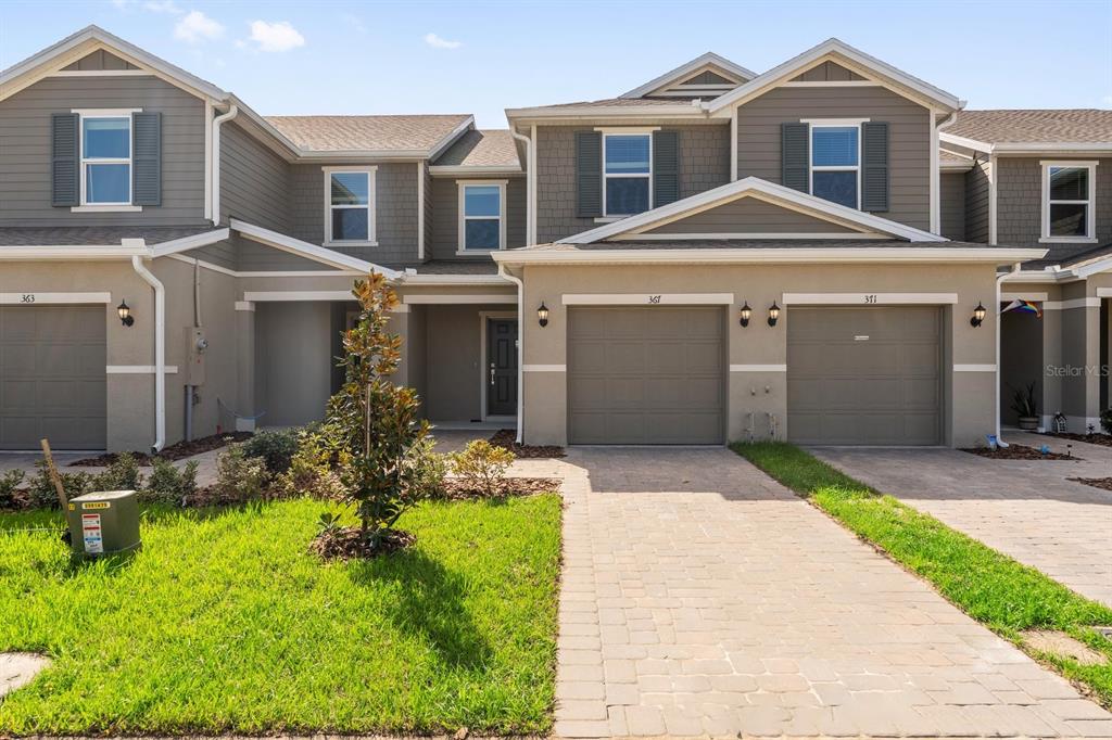The exterior of a multi-unit townhouse complex features beige stucco walls, gray siding, and garages — 367 SEQUOIA DRIVE, LAKE WALES, FL