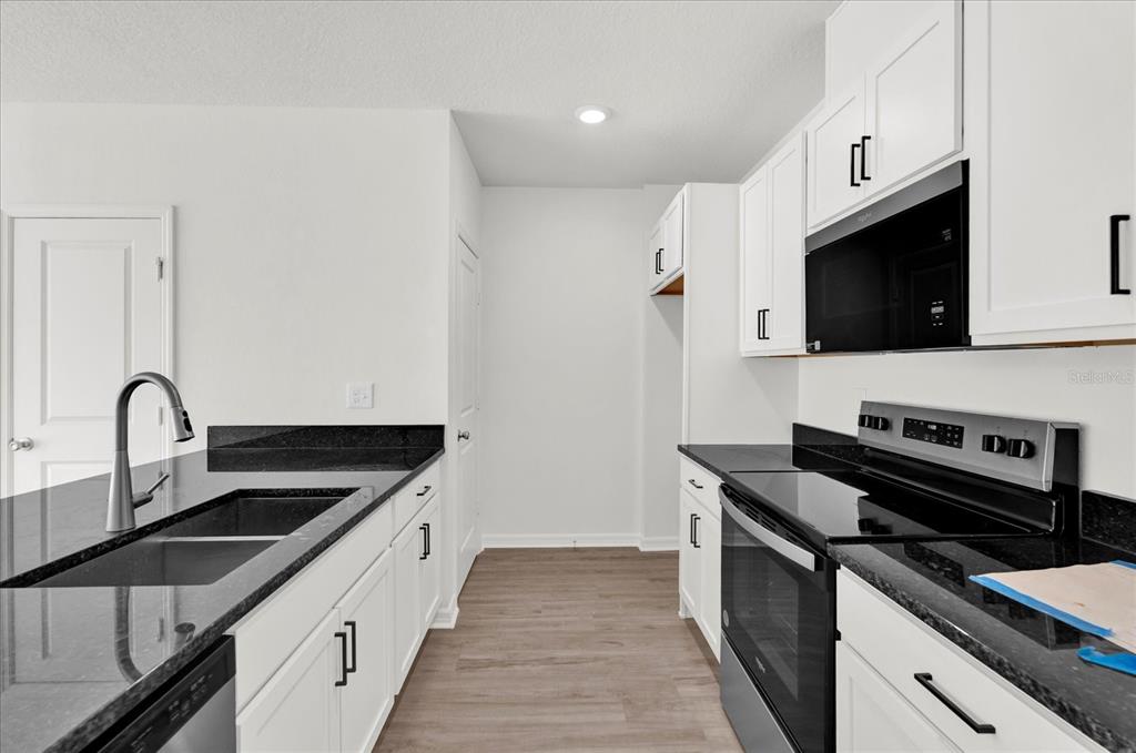 A kitchen features white cabinets, black granite countertops, stainless steel appliances, and wood-look flooring — 367 SEQUOIA DRIVE, LAKE WALES, FL