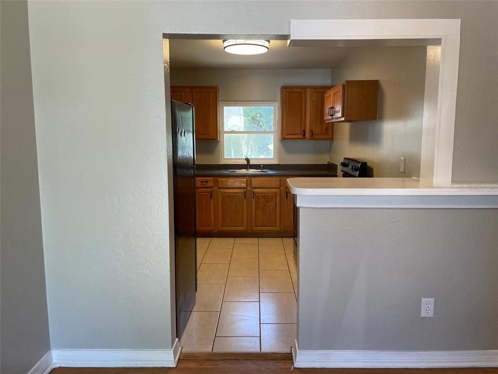 A kitchen with wooden cabinets, tile flooring, and a pass-through window to an adjacent room — 320 W GRAVES AVENUE, ORANGE CITY, FL