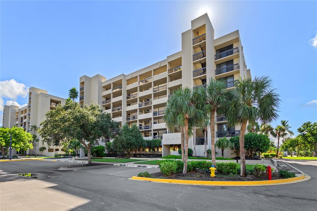A multi-story beige apartment building stands behind a parking lot with palm trees — 1065 GULF OF MEXICO DRIVE UNIT 402, LONGBOAT KEY, FL