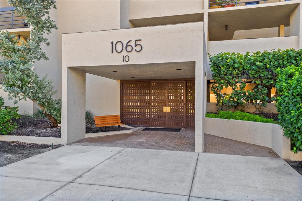 An exterior view of a building entrance with a covered walkway and brown metal doors — 1065 GULF OF MEXICO DRIVE UNIT 402, LONGBOAT KEY, FL