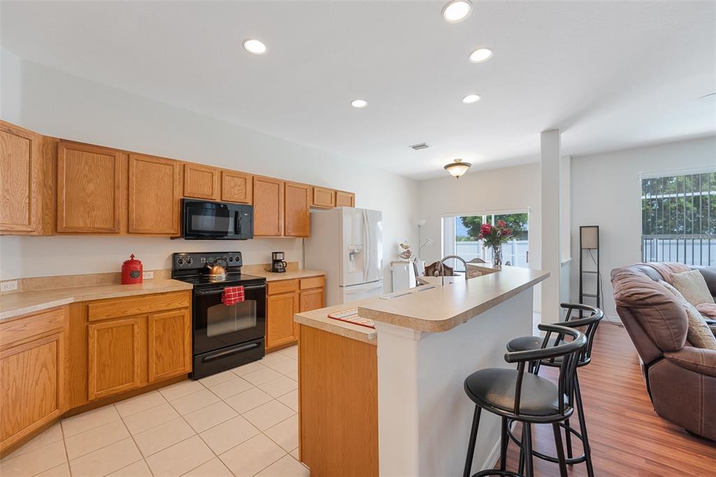 A kitchen with oak cabinets, black appliances, and a breakfast bar overlooking a living area — 1709 NW 15TH TERRACE, CAPE CORAL, FL