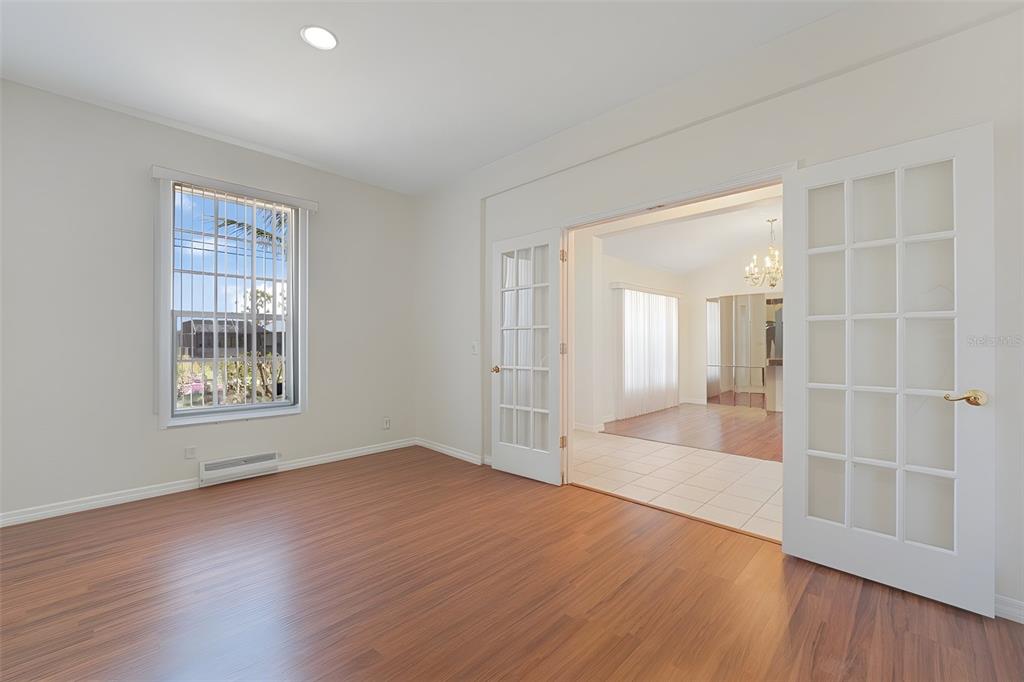 A room with wood-look flooring and a window leads through French doors to another room — 1709 NW 15TH TERRACE, CAPE CORAL, FL