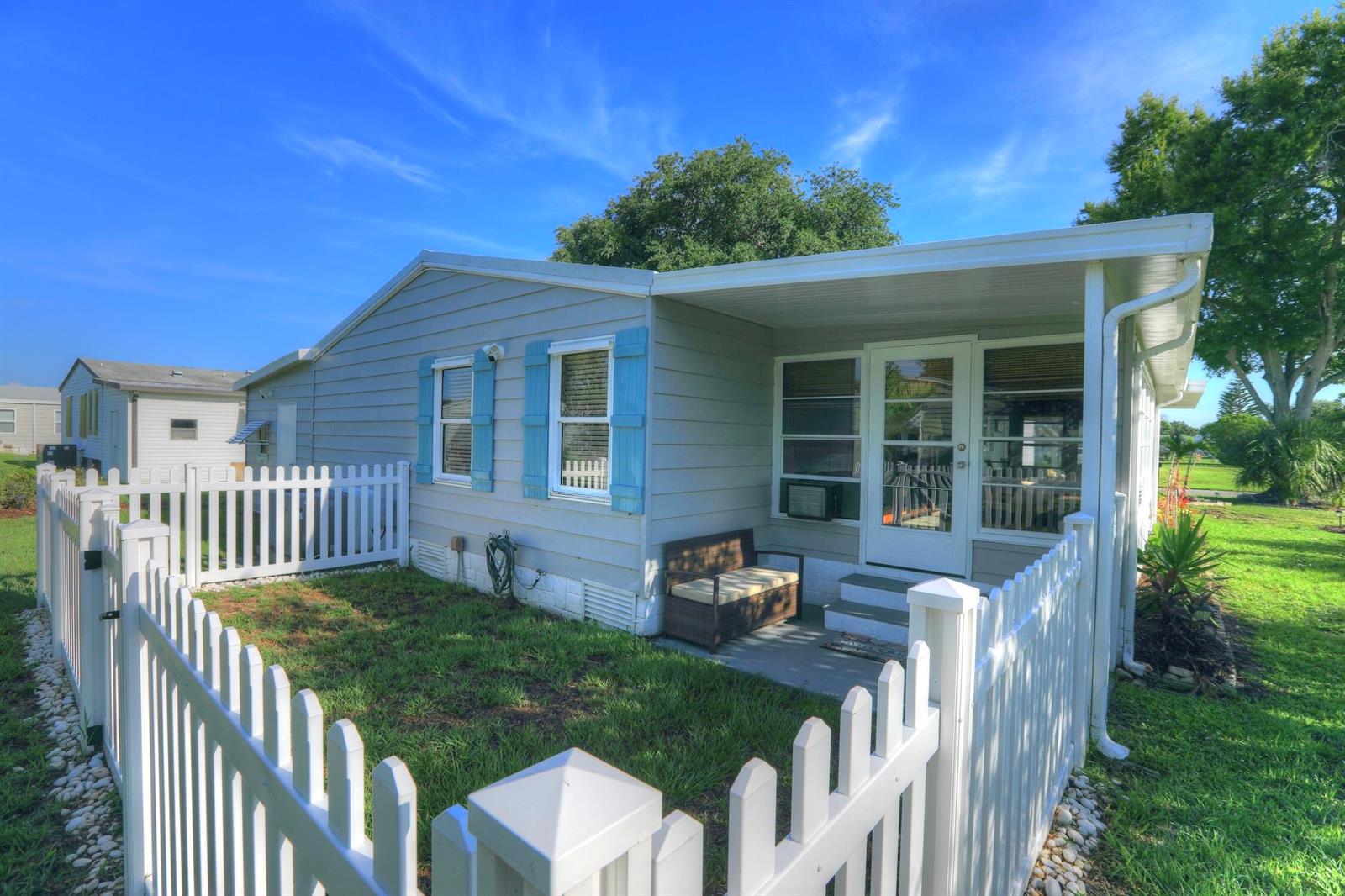 A light gray mobile home with blue shutters and a white picket fence — BAREFOOT BAY, FL