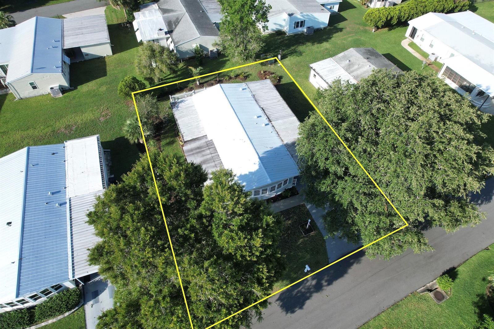 An aerial view shows a single-story house with a metal roof and surrounding trees — BAREFOOT BAY, FL