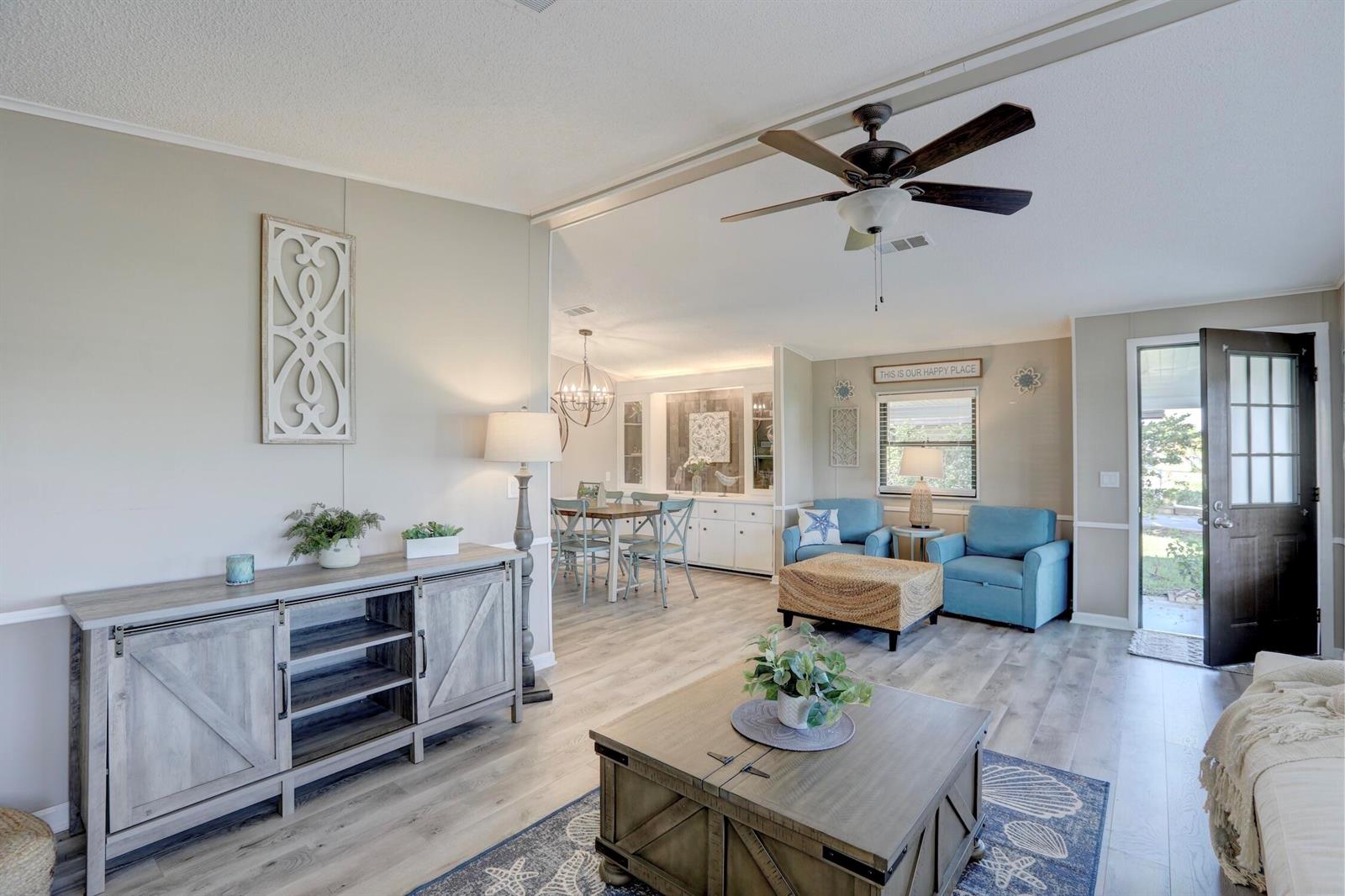 A living room with wood-look flooring, a ceiling fan, and blue armchairs near the entrance — BAREFOOT BAY, FL