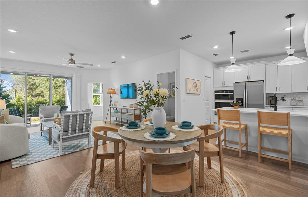 An open-concept kitchen, dining area, and living room featuring light wood floors and white cabinetry — 227 MISTY HARBOR TRACE, PALM COAST, FL