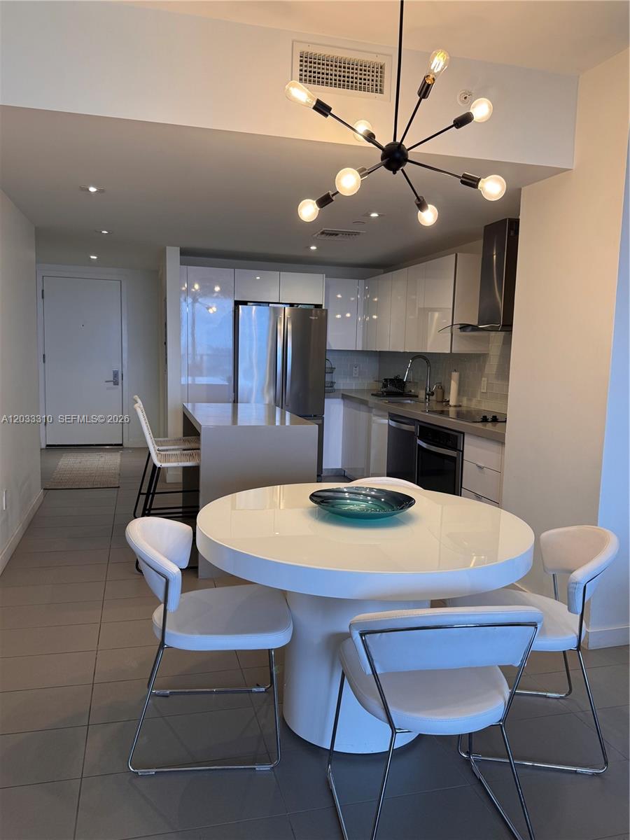 A modern kitchen with white cabinetry and a round dining table sits in an open-concept space — 1600 NE 1st Ave # 2015, Miami FL 33132, MIAMI, FL