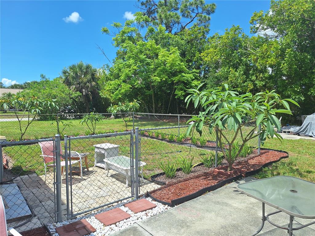 A fenced backyard features a paved patio, a small garden bed, and mature trees — 402 CICERO STREET NW, PORT CHARLOTTE, FL