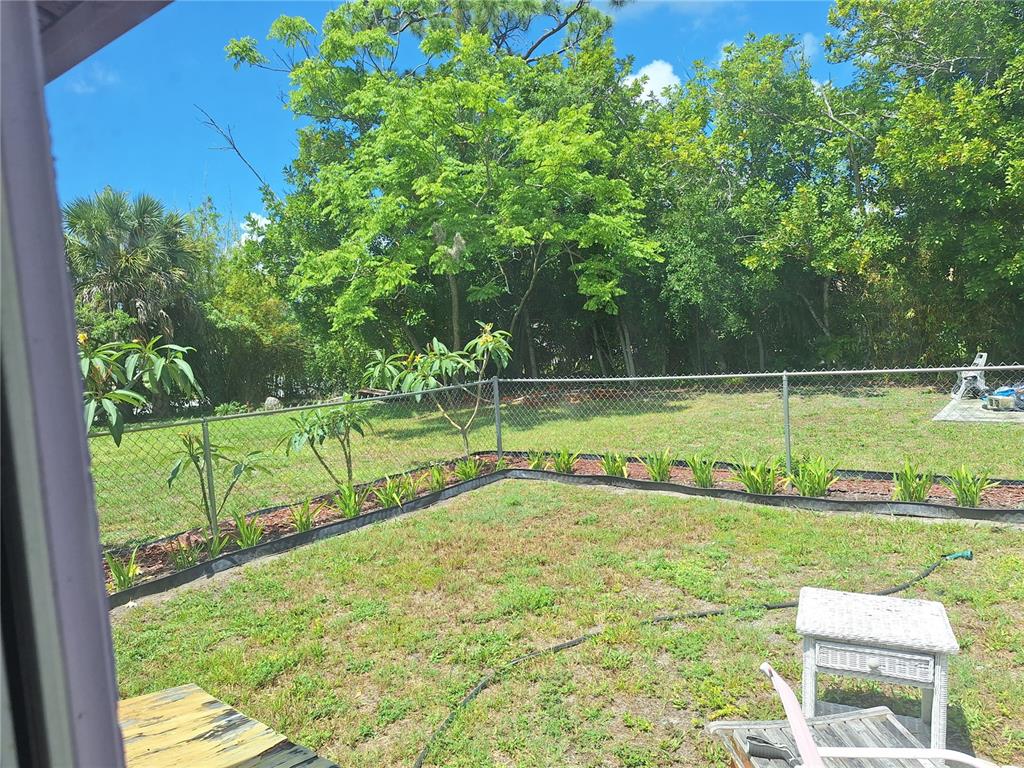 A fenced backyard features a grassy lawn, small planted shrubs, and mature trees — 402 CICERO STREET NW, PORT CHARLOTTE, FL
