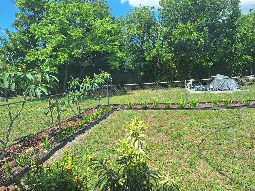 A backyard features a chain-link fence, a garden bed with small plants, and mature trees — 402 CICERO STREET NW, PORT CHARLOTTE, FL
