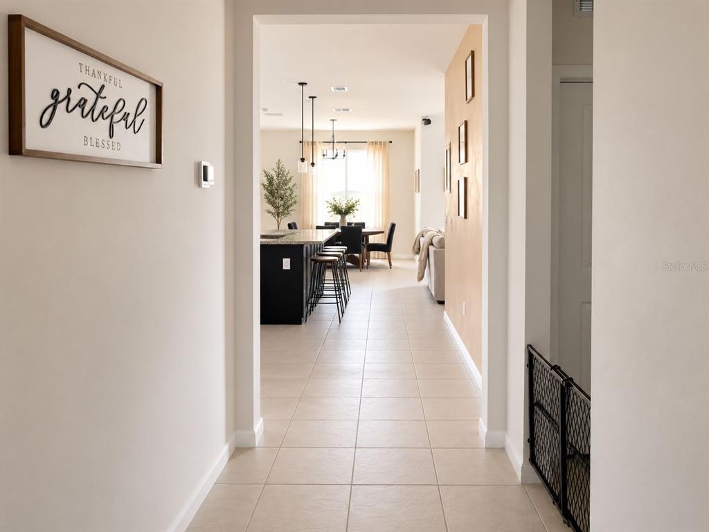 A tiled hallway leads into an open-concept kitchen and dining area with modern lighting — 1051 PATRIOT LOOP, HAINES CITY, FL