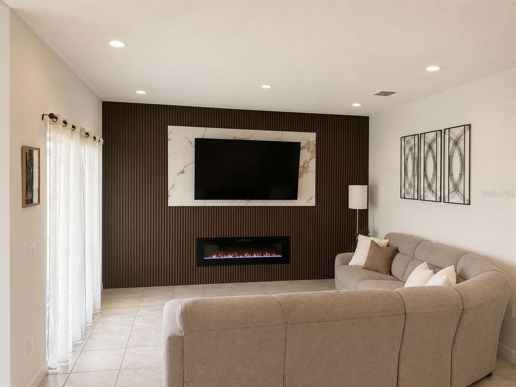 A living room features a slatted dark wood accent wall with a fireplace and television — 1051 PATRIOT LOOP, HAINES CITY, FL