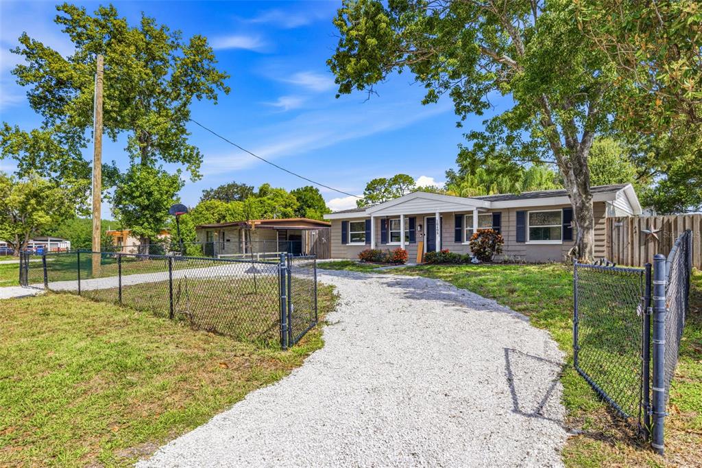 A single-story house with a gravel driveway and a chain-link fence under a blue sky — 10408 VENTURA AVENUE, TAMPA, FL