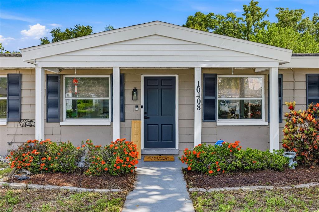 The exterior of a single-story house features a dark blue front door and orange flowers — 10408 VENTURA AVENUE, TAMPA, FL