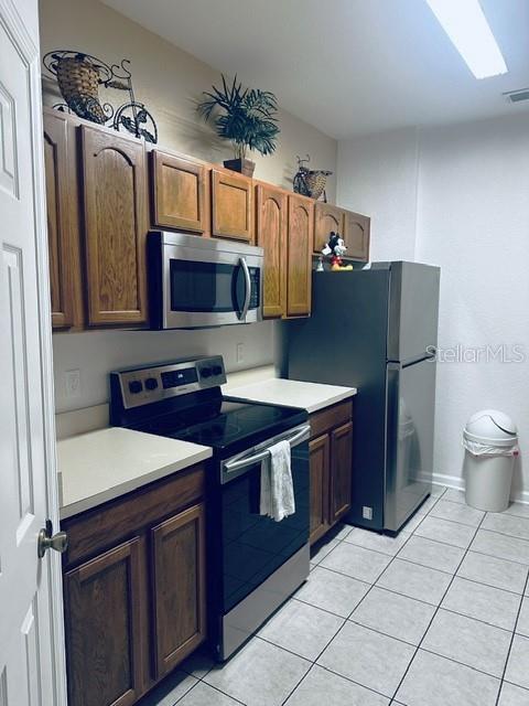 A kitchen features wooden cabinets, stainless steel appliances, and light-colored countertops over tiled floors — 2785 ALMATON LOOP UNIT 103, KISSIMMEE, FL
