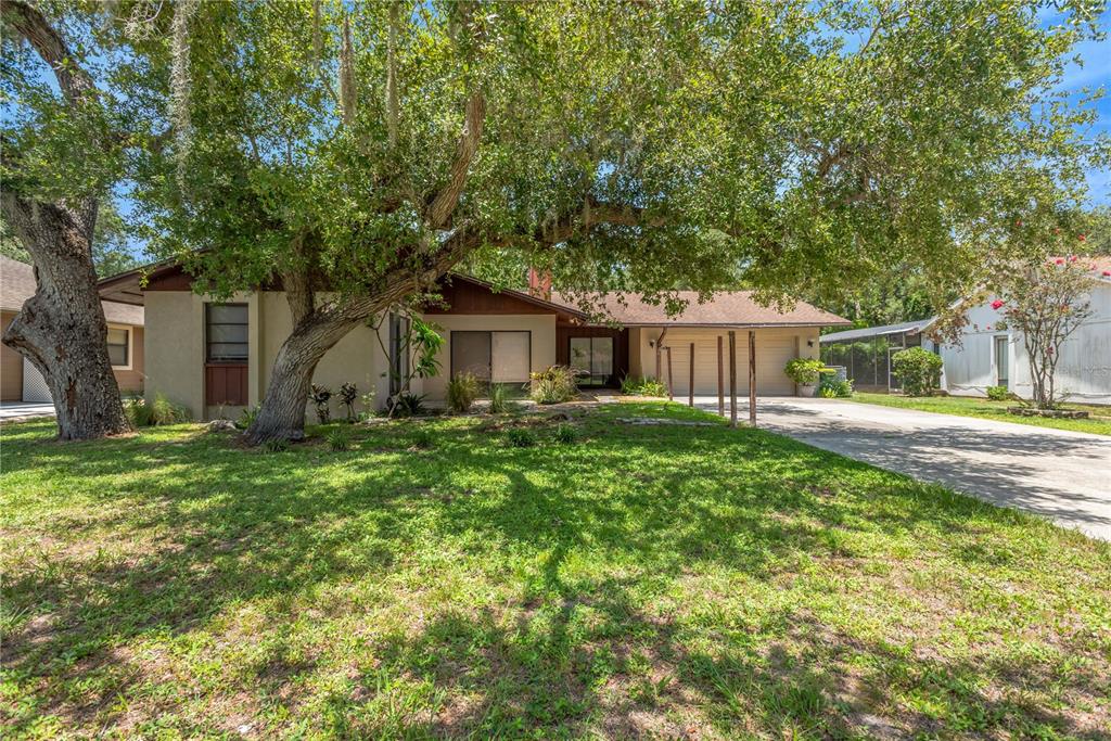 A single-story house with a brown roof, tan exterior, and a large tree in front — 213 WHISPERING OAKS COURT, SARASOTA, FL