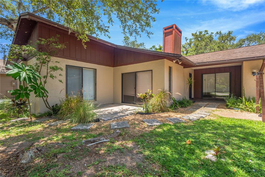 A backyard view of a house with a patio, sliding glass doors, and a chimney — 213 WHISPERING OAKS COURT, SARASOTA, FL