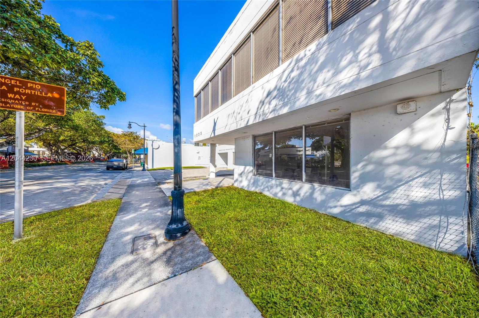 A low-angle exterior view shows a white building with large windows and a sidewalk — 1235 SW 22nd St, Miami FL 33145, MIAMI, FL