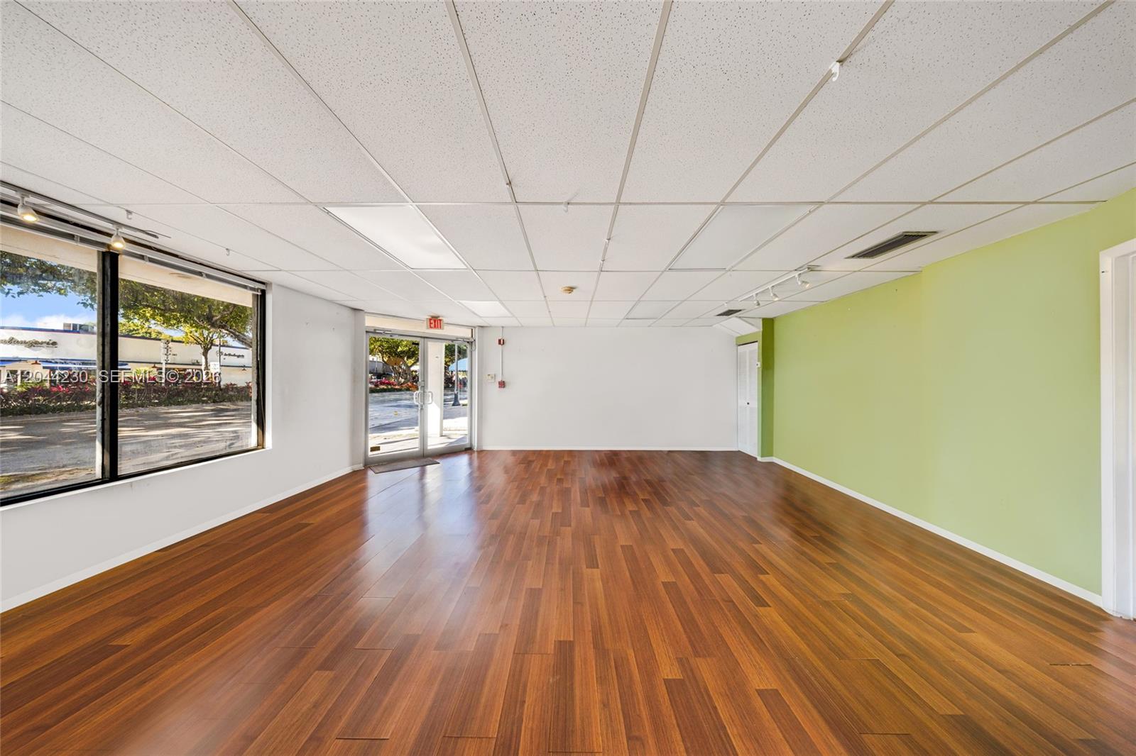 An empty commercial space features wood-look flooring, a drop ceiling, and a lime green wall — 1235 SW 22nd St, Miami FL 33145, MIAMI, FL