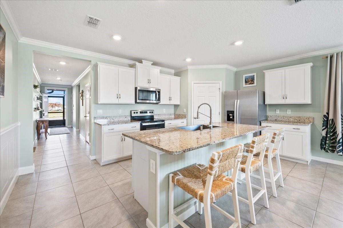 A kitchen with white cabinets, granite countertops, a center island, and light-colored tile flooring — 7499 Tourmaline, Grant Valkaria FL 32949, GRANT VALKARIA, FL