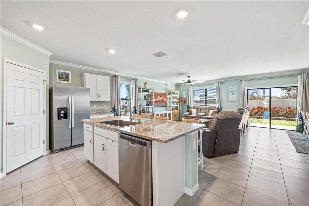 A kitchen with white cabinets and granite countertops opens into a living area with tile floors — 7499 Tourmaline, Grant Valkaria FL 32949, GRANT VALKARIA, FL