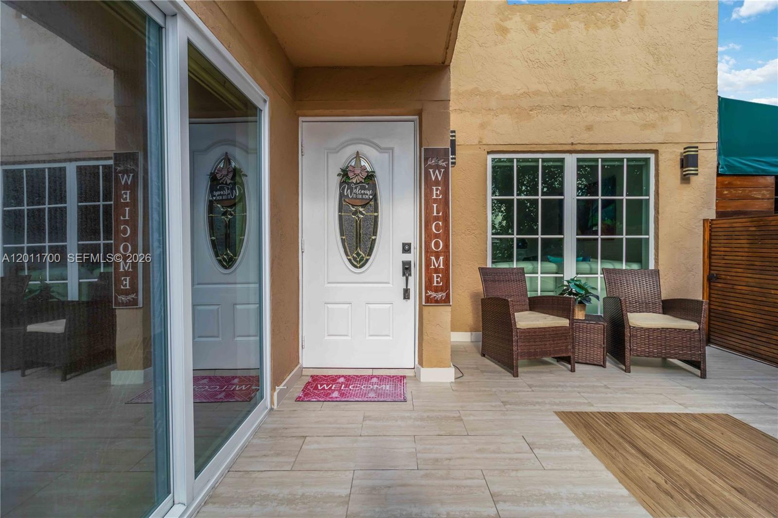 A white front door with a decorative sign sits on a tiled patio with seating — 11880 SW 19th Ln # 165, Miami FL 33175, MIAMI, FL
