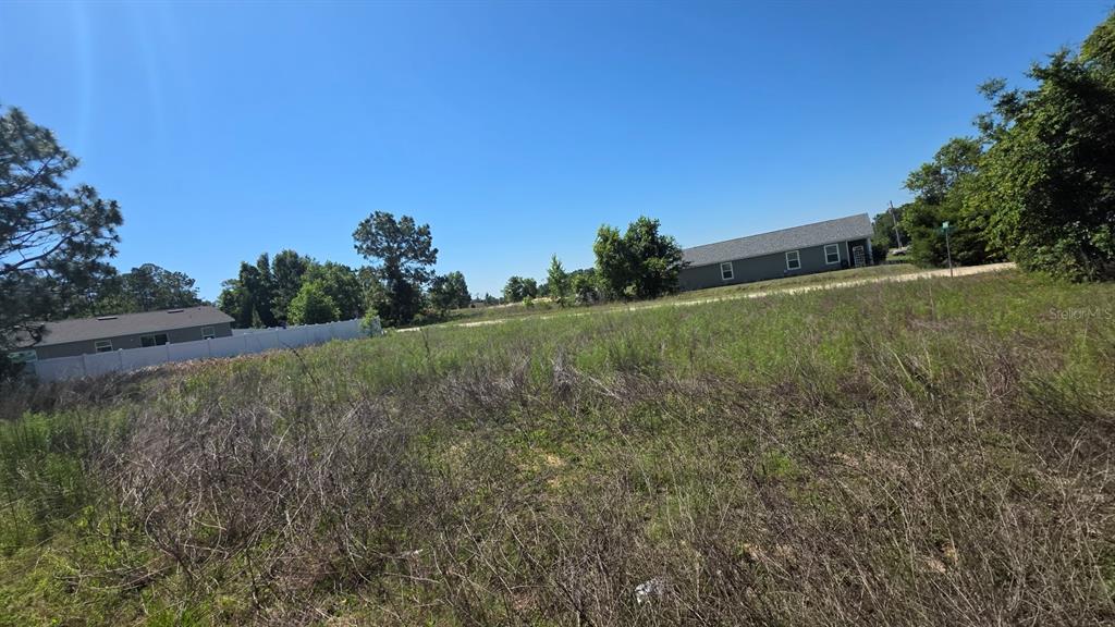 A vacant, grassy lot sits in front of a residential house and a white fence — SW 149TH TERRACE, OCALA, FL