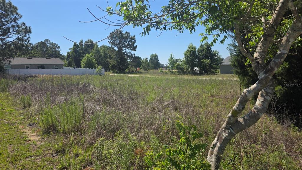A vacant, grassy lot is shown with a white fence and nearby houses in the background — SW 149TH TERRACE, OCALA, FL