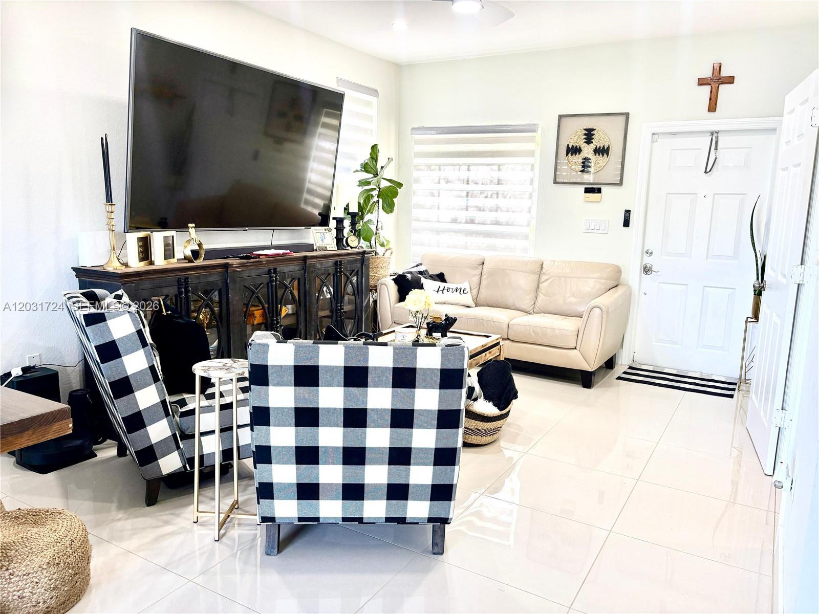 A living room features a large television, two buffalo-check armchairs, and a beige sofa — PEMBROKE PINES, FL