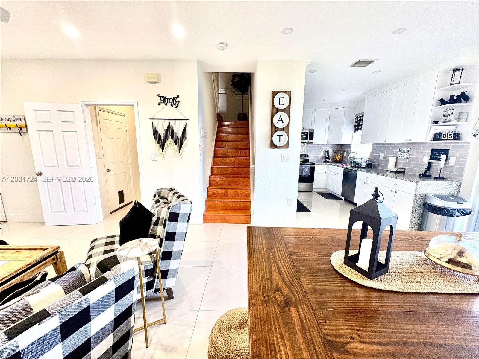 A bright interior features a living area with checkered chairs, wooden stairs, and a kitchen — PEMBROKE PINES, FL