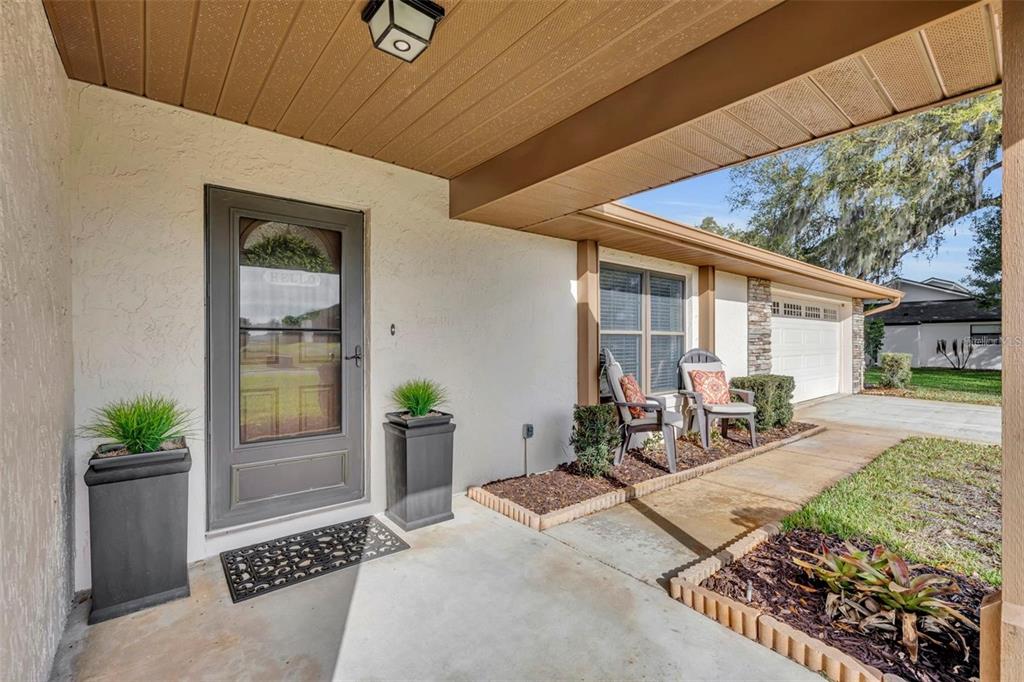 A covered concrete porch features a front door, two planters, and two chairs — 3158 WHISPER WIND DRIVE, ST CLOUD, FL