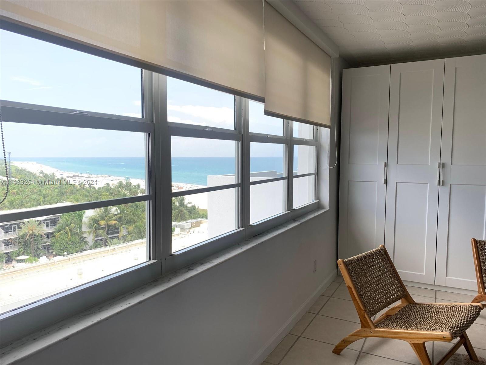 A room with white cabinets, a woven chair, and a large window overlooking the ocean — 100 Lincoln Rd # 1039, Miami Beach FL 33139, MIAMI BEACH, FL