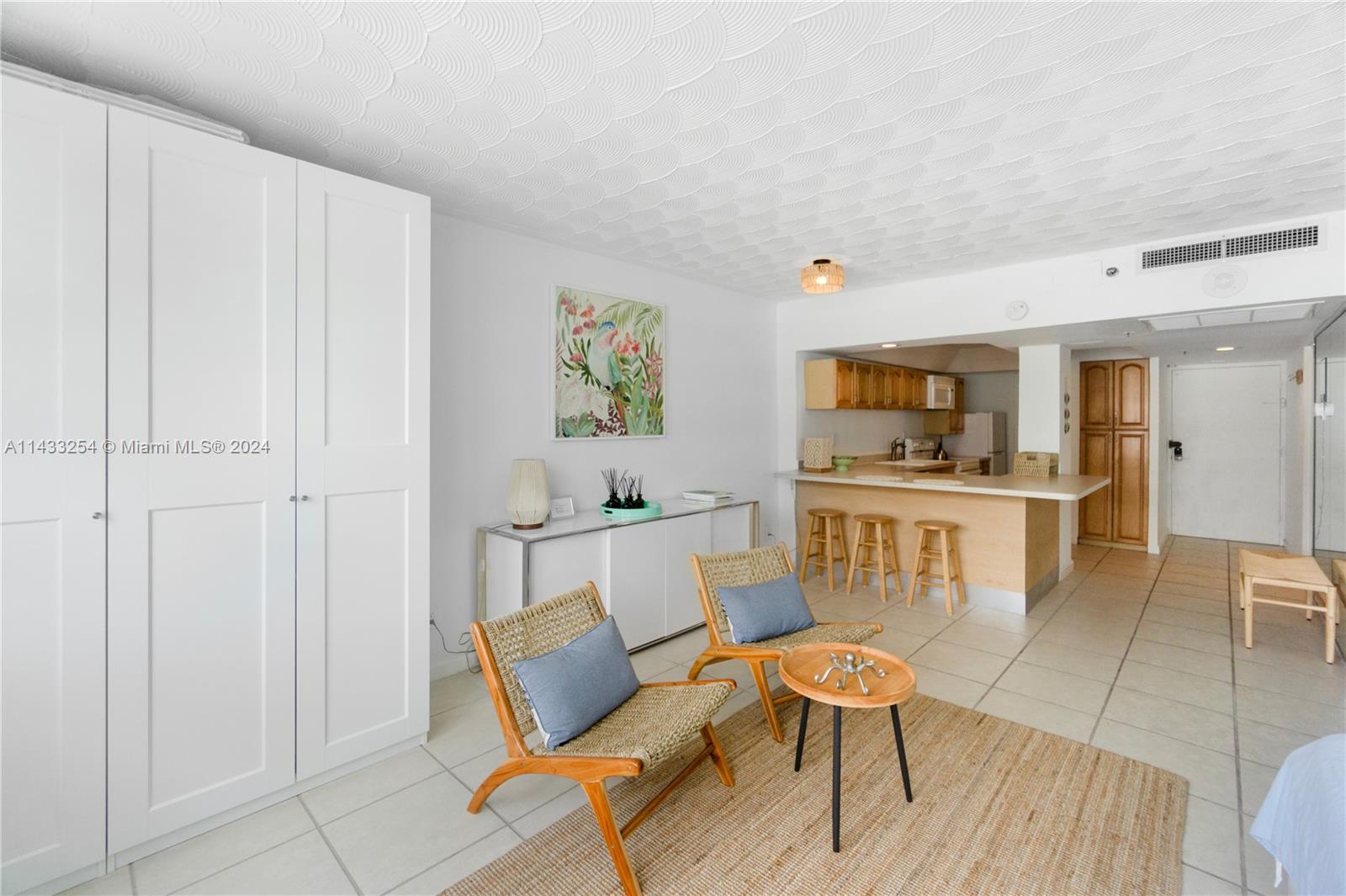 This living area features a white wardrobe, two woven chairs, and an open kitchen counter — 100 Lincoln Rd # 1039, Miami Beach FL 33139, MIAMI BEACH, FL