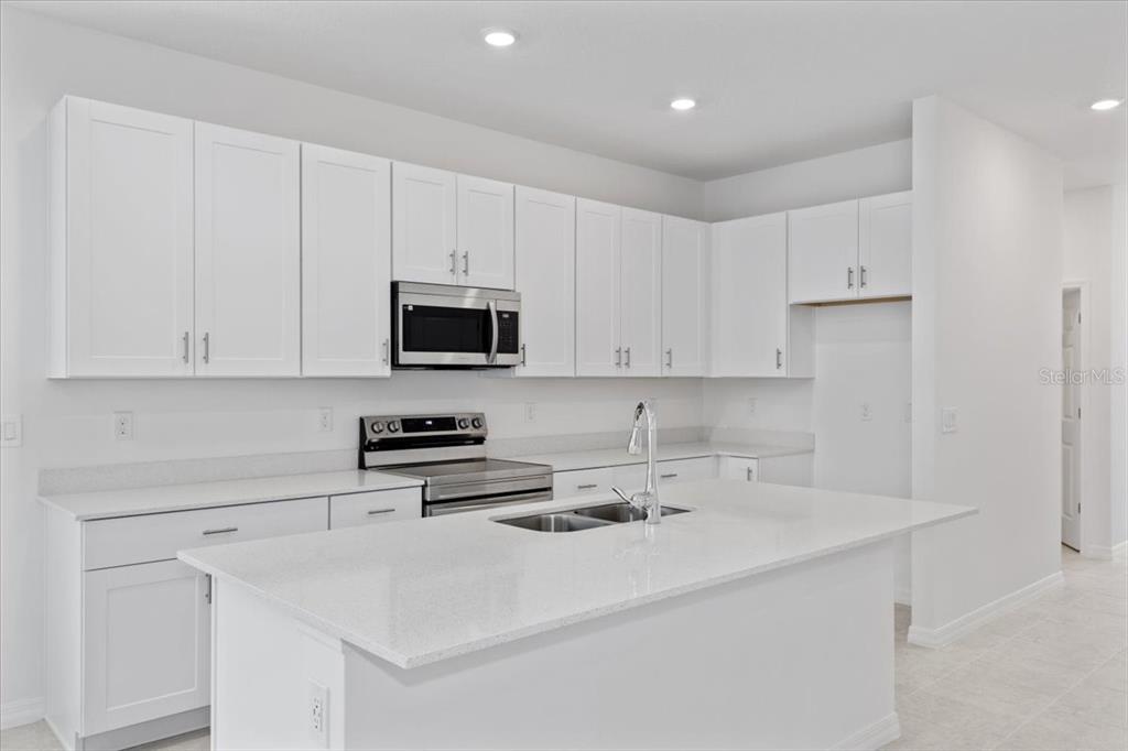 A modern kitchen features white cabinets, stainless steel appliances, and a large quartz-topped island — 1198 ATLANTIC AVENUE, FRUITLAND PARK, FL