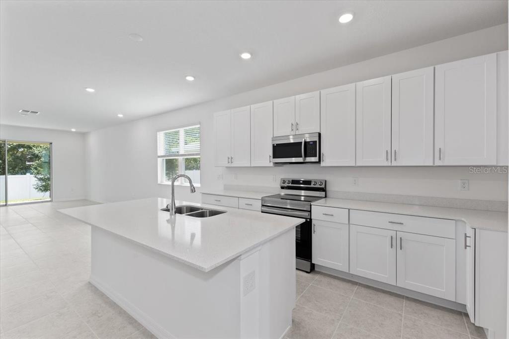 A modern kitchen features white cabinets, quartz countertops, a center island, and stainless steel appliances — 1198 ATLANTIC AVENUE, FRUITLAND PARK, FL