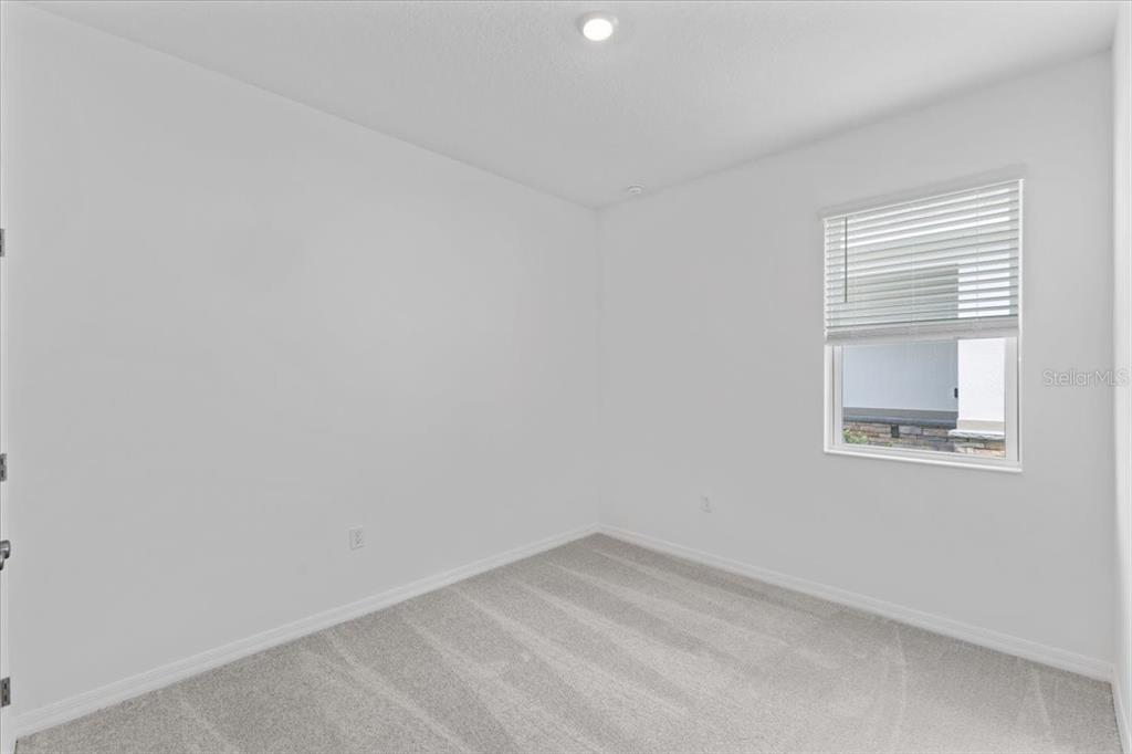 An empty bedroom features white walls, gray carpet, and a window with white blinds — 1198 ATLANTIC AVENUE, FRUITLAND PARK, FL
