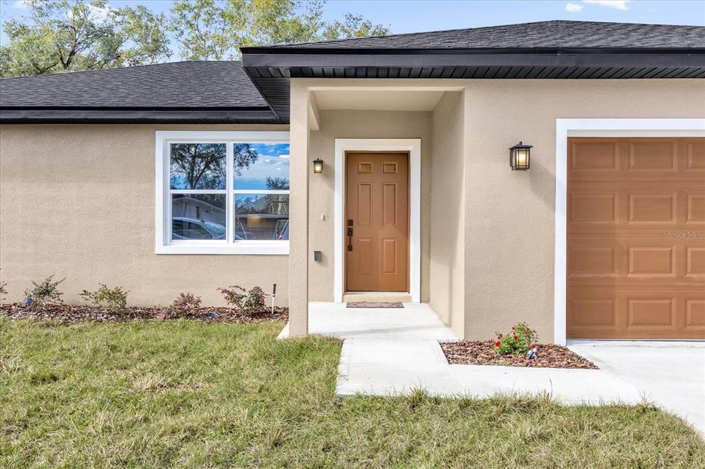 The exterior of a tan house features a brown front door and a garage door — 16440 SE 87TH COURT, SUMMERFIELD, FL