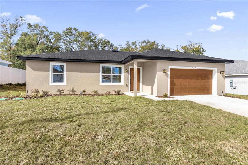 A single-story house with tan stucco siding, a dark roof, and a two-car garage — 16440 SE 87TH COURT, SUMMERFIELD, FL